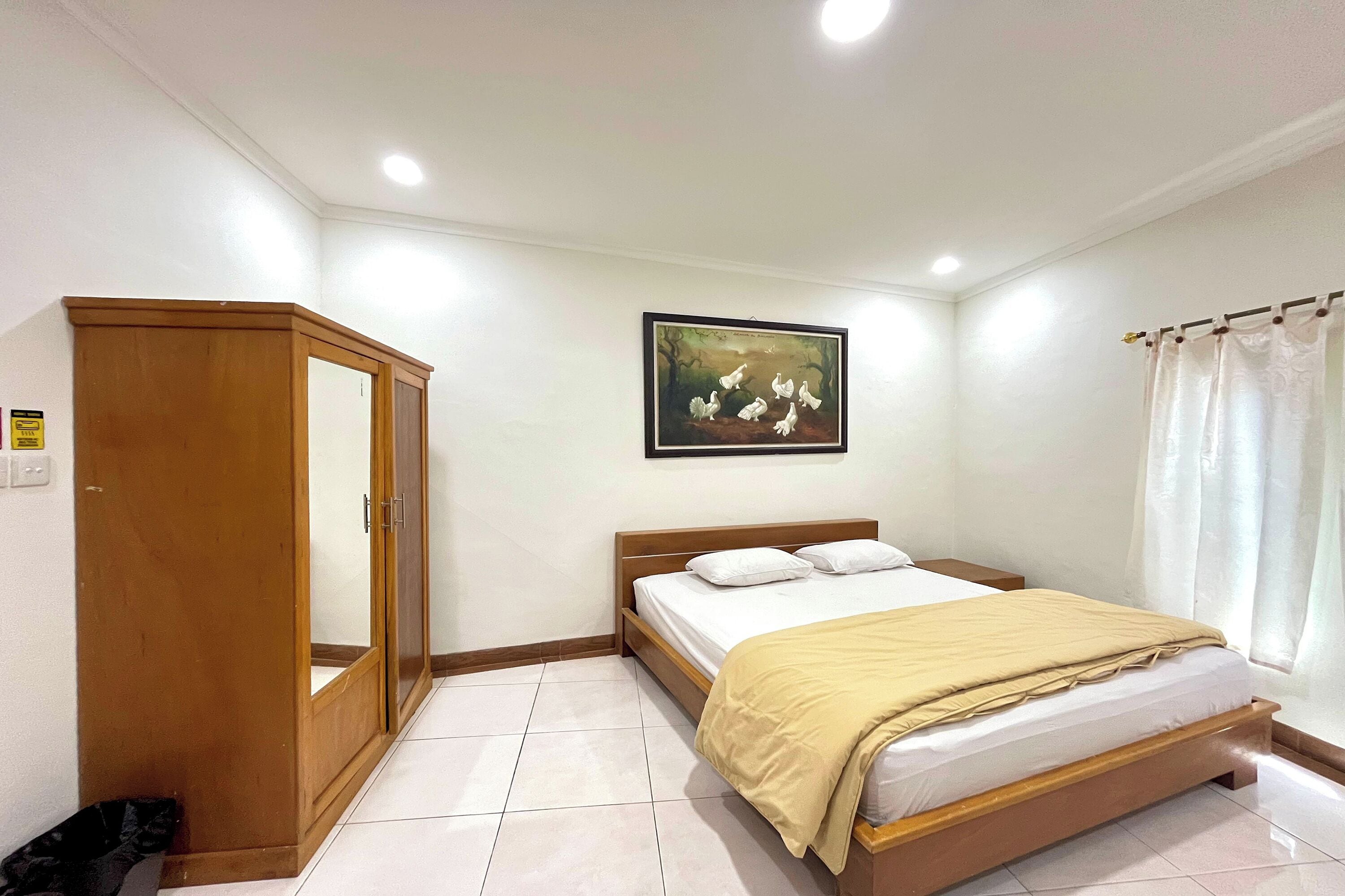 Un dormitorio ordenado con cama, armario de madera, un cuadro en la pared y una cortina.