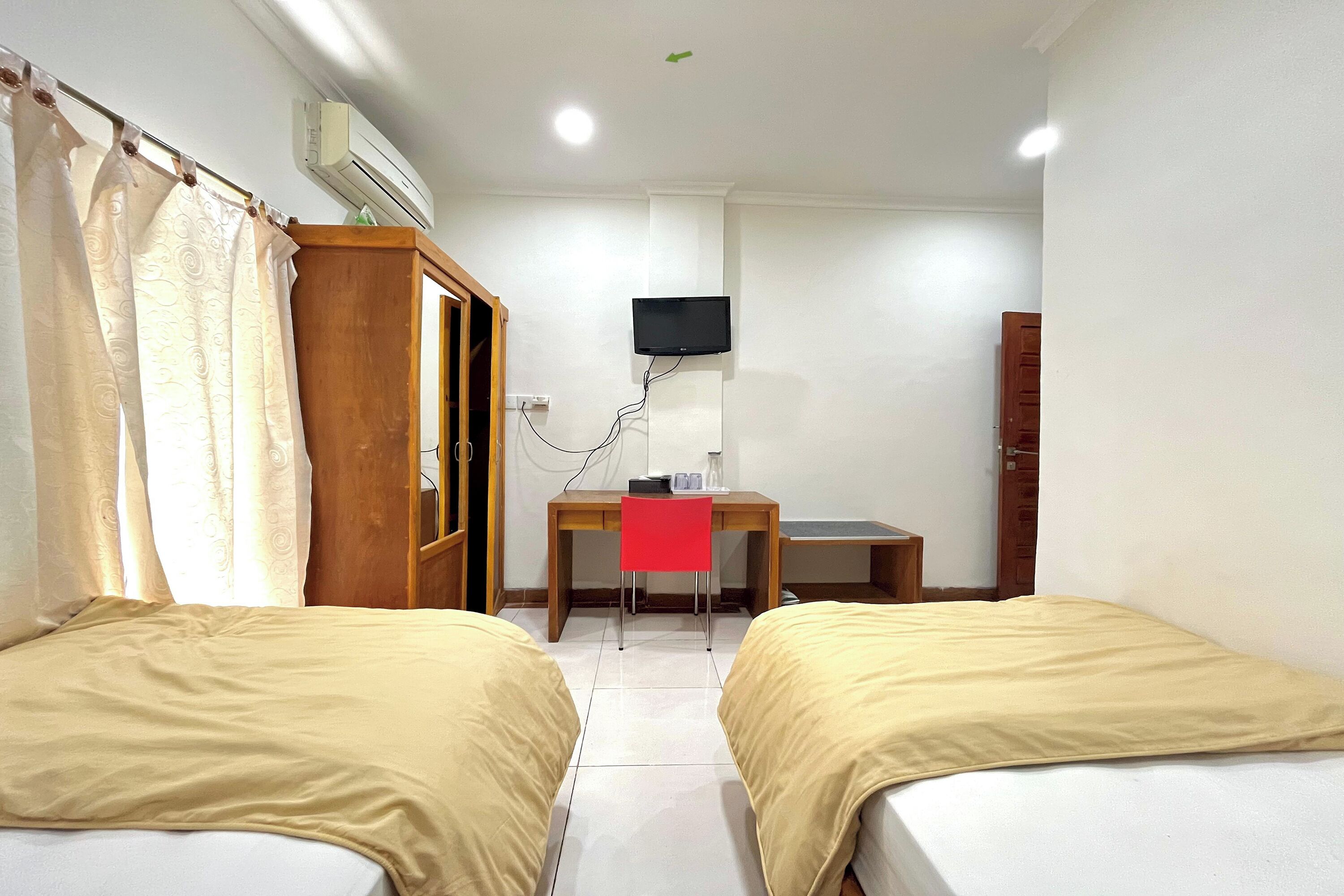 Ein Hotelzimmer mit zwei Betten, einem Schreibtisch, einem Stuhl, einem Fernseher und einer Klimaanlage.