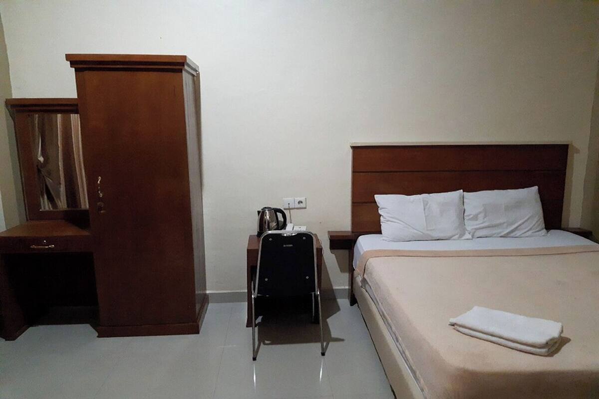 Une chambre d’hôtel avec un lit, une armoire, un bureau et une valise.