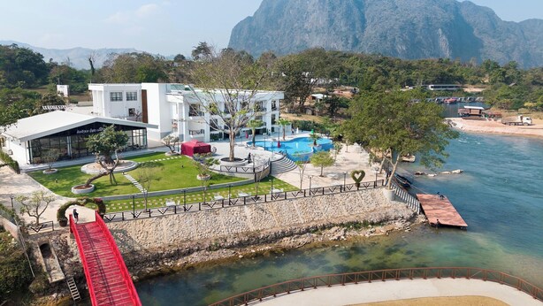 A modern hotel with a swimming pool, a red bridge, and a mountainous backdrop. - Daoneua Riverside Resort (Muang Fuang)
