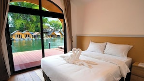A hotel room with a large bed, a wooden floor, and a view of a water body with boats. - Daoneua Riverside Resort (Muang Fuang)
