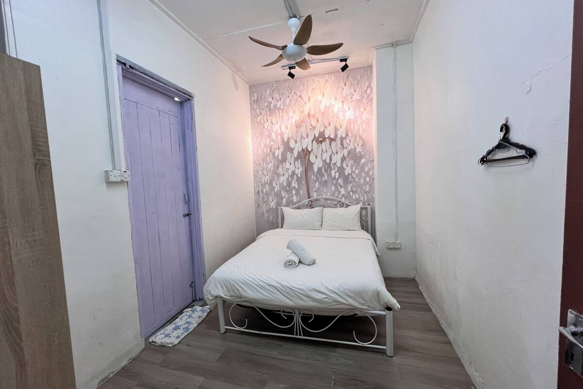 A bedroom with a bed, a ceiling fan, a door, and a wall with a decorative pattern.