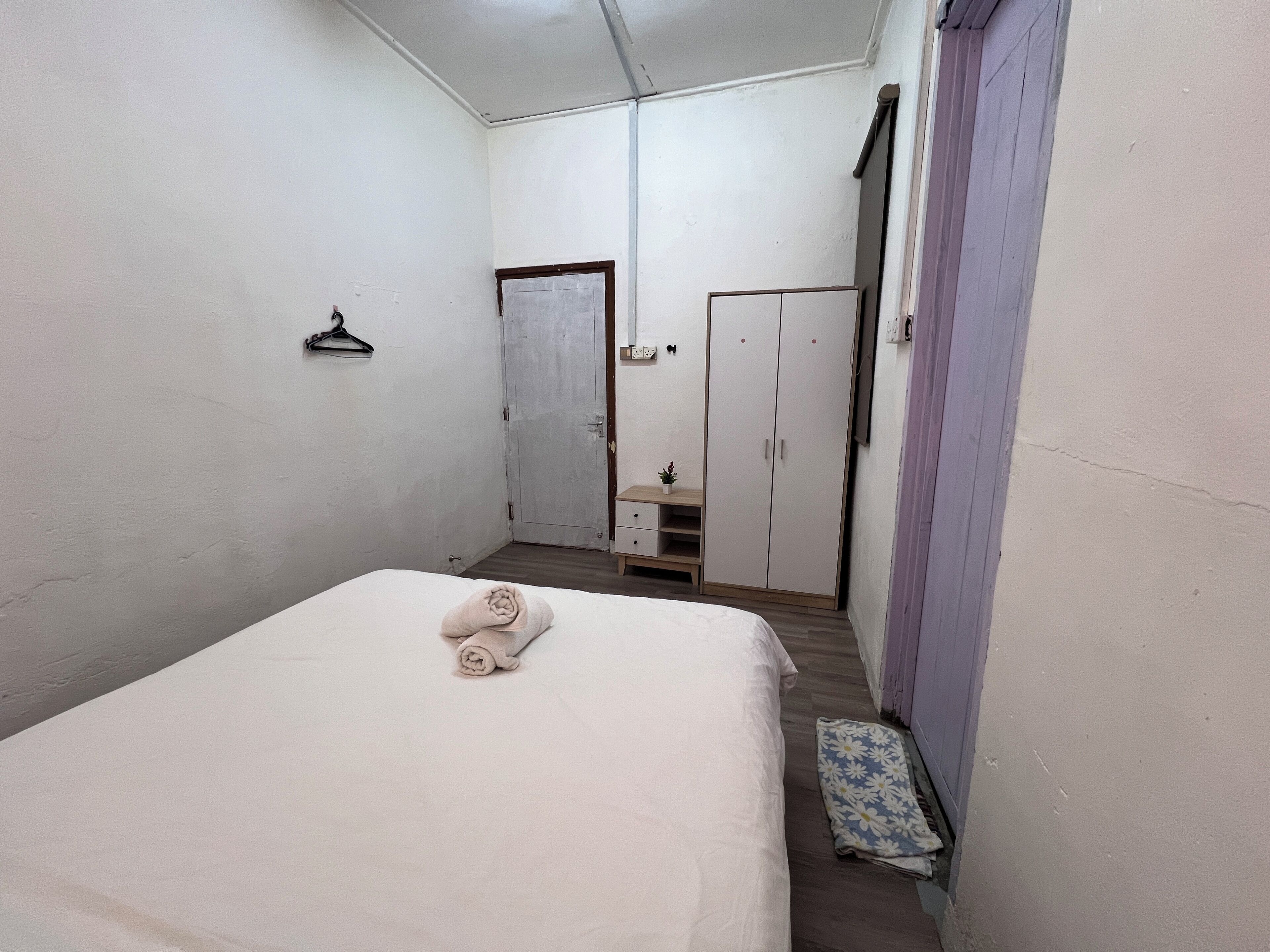 Une petite pièce propre, avec un lit simple, une armoire, une petite table et une porte donnant sur une autre pièce.
