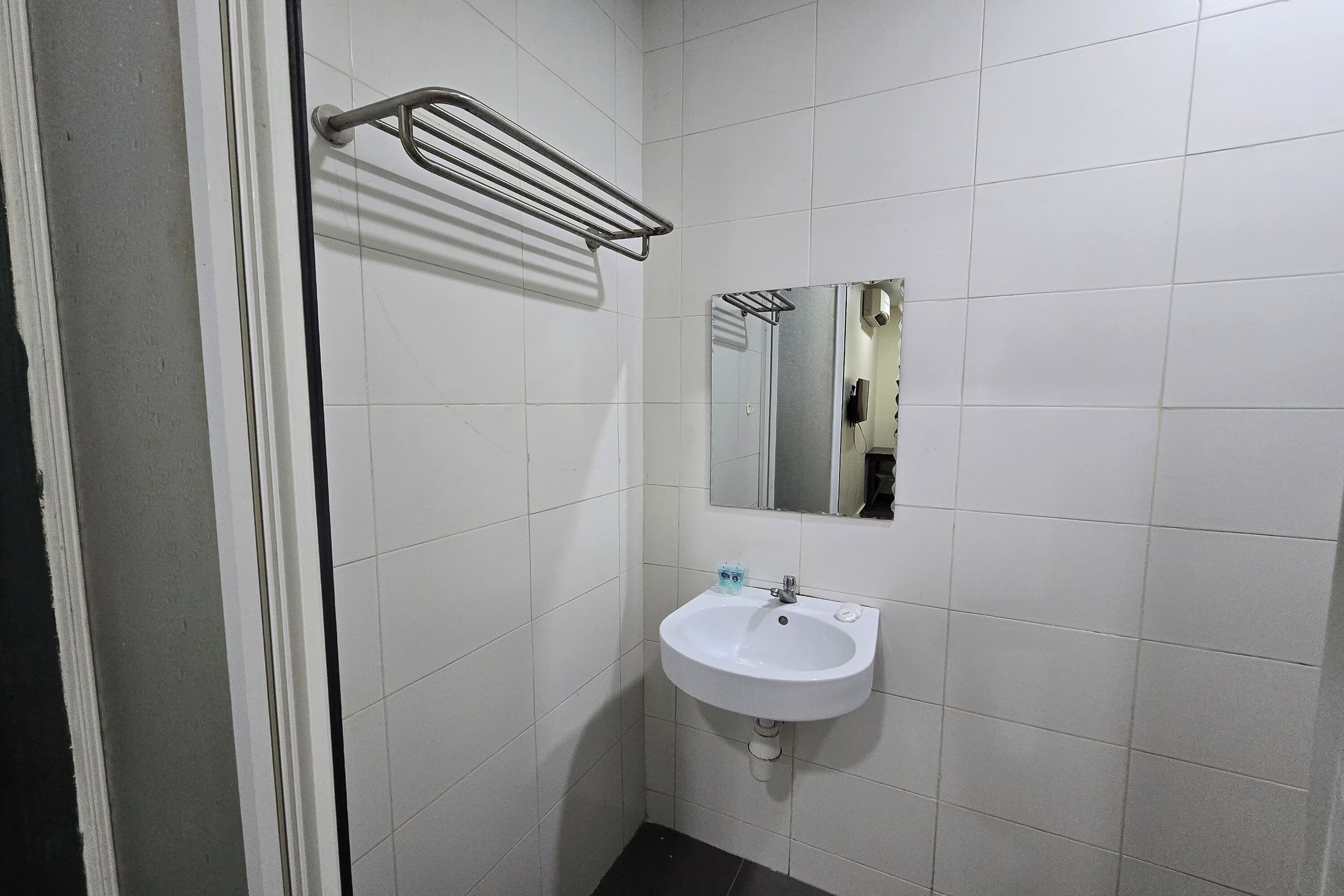 Een badkamer met witte betegelde wanden, een witte wastafel met spiegel erboven en een handdoekrek.