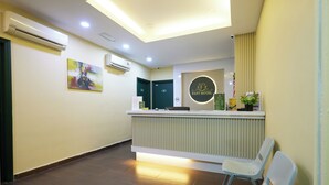 Zona de recepción de un hotel, con mostrador, una silla de espera y un cartel en la pared.