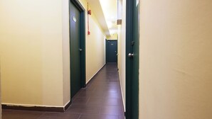 Un pasillo con puertas a ambos lados, suelo de baldosas y una lámpara en el techo.