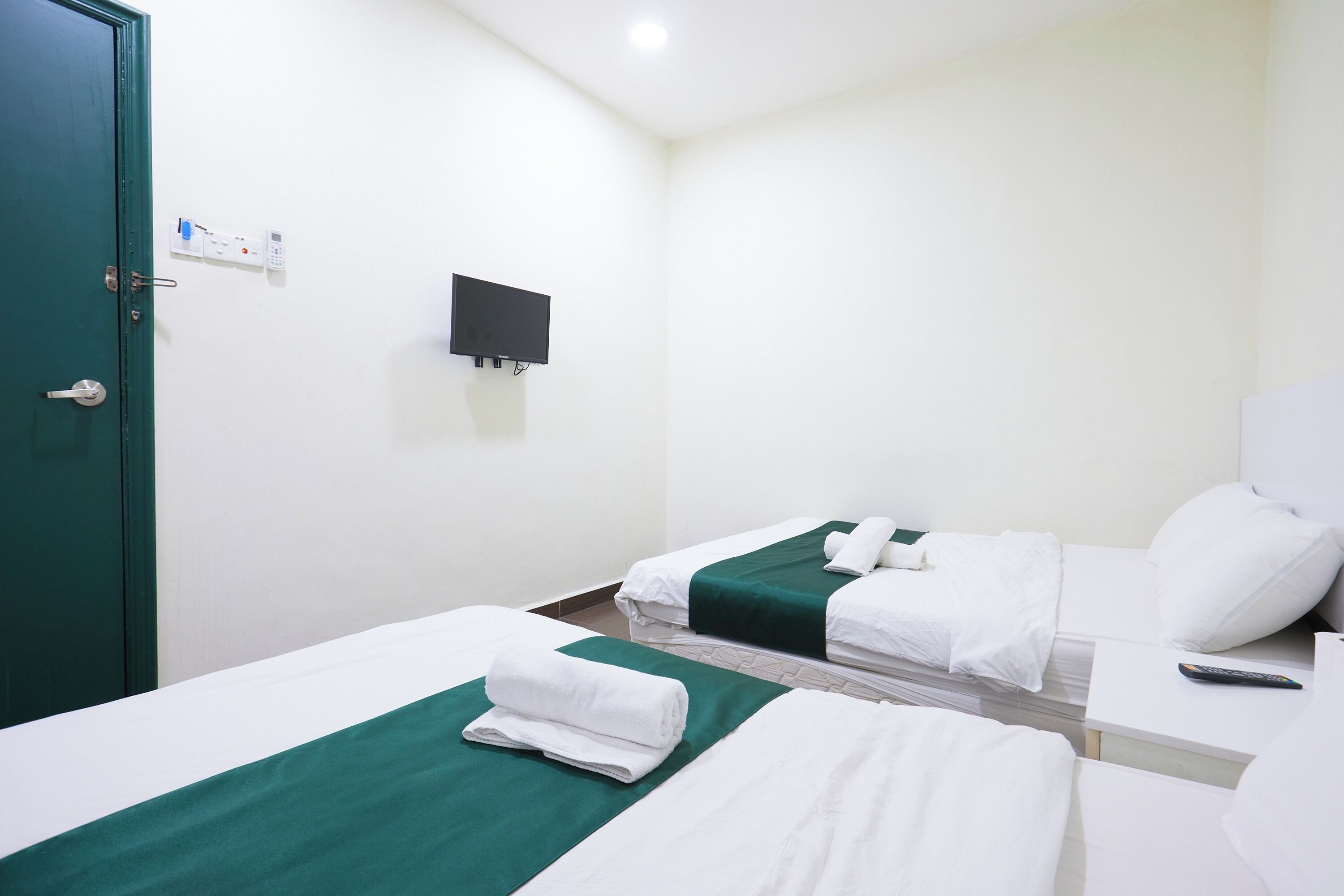 A hotel room with two beds, a TV, a door, and a control panel on the wall.
