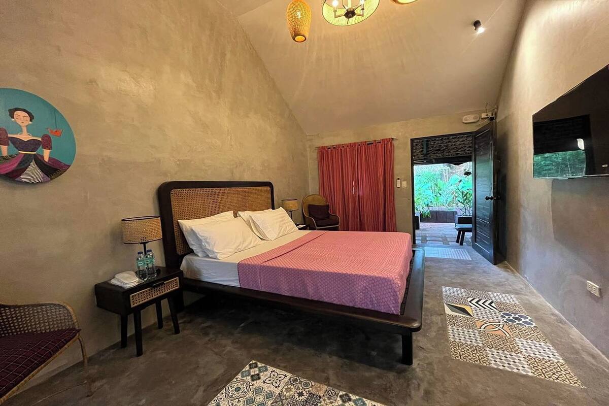 A bedroom with a bed, bedside tables, a wall-mounted artwork, a patterned rug, and a view of the outdoors.