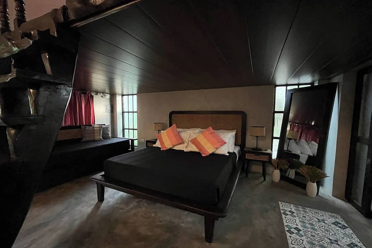 A bedroom with a large bed, a wooden headboard, a nightstand, a mirror, and a window with curtains.