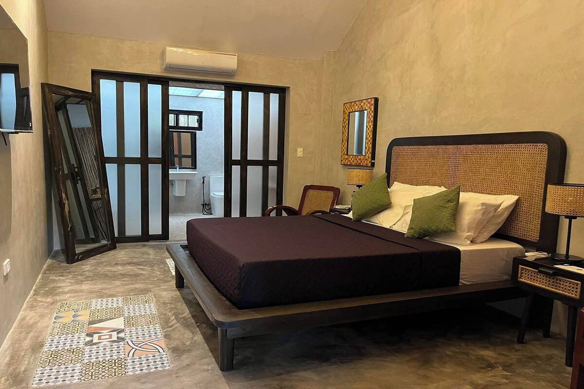 A bedroom with a bed, a nightstand, a mirror, and a door leading to a bathroom.