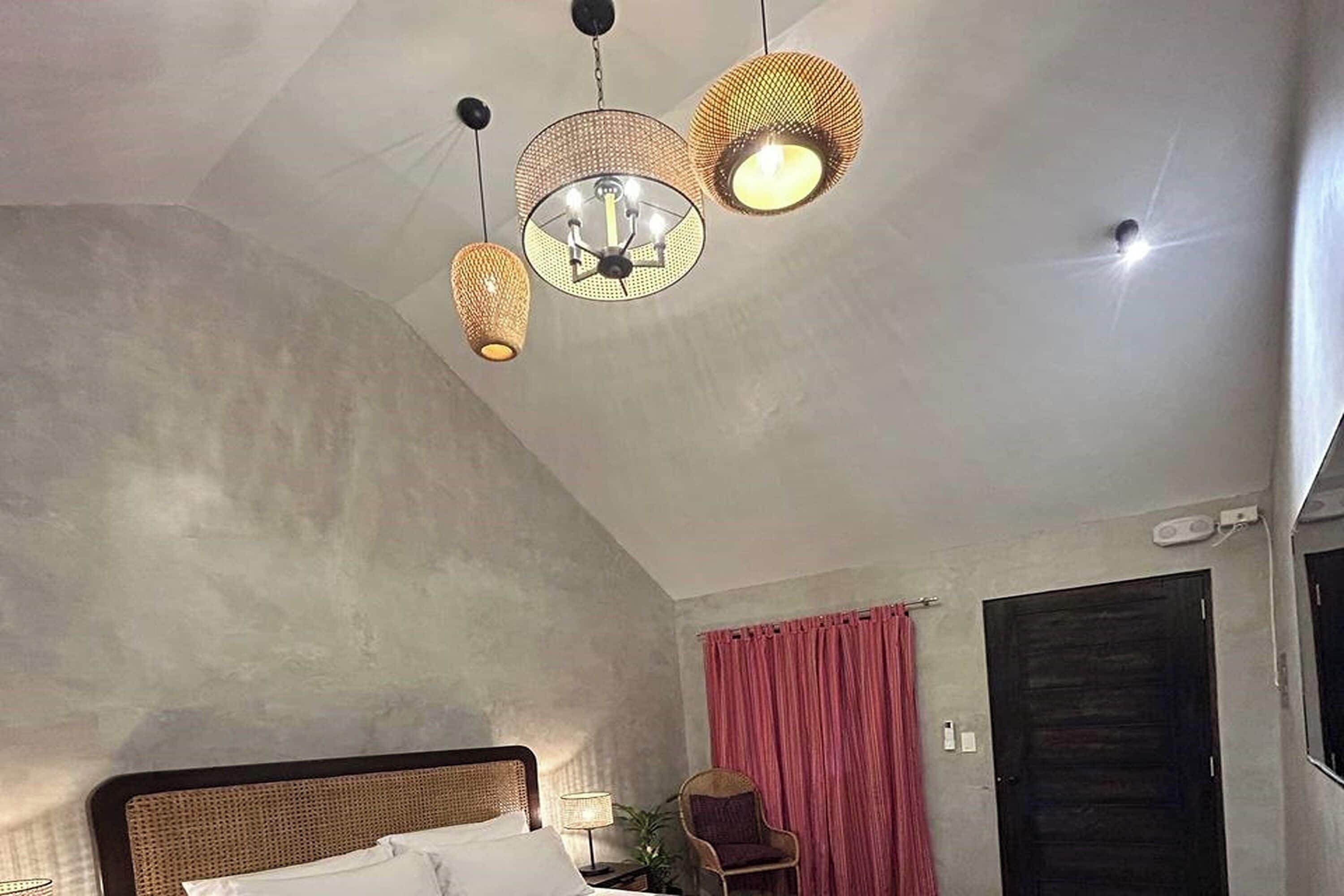 Une chambre d’hôtel avec un lit, une chaise, un rideau rouge et un luminaire au plafond.