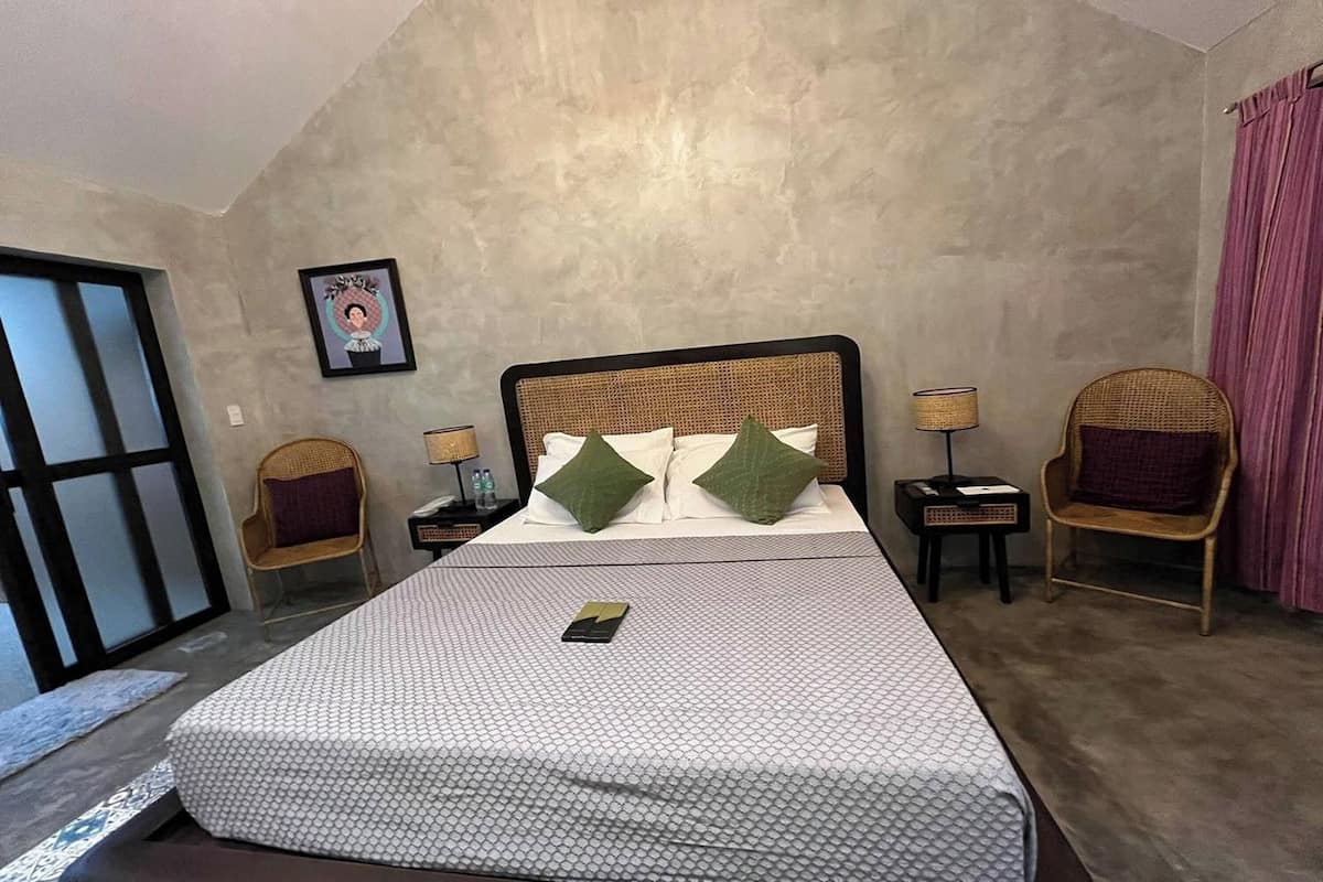 A hotel room with a large bed, two nightstands, two wicker chairs, a framed picture on the wall, and a sliding door.