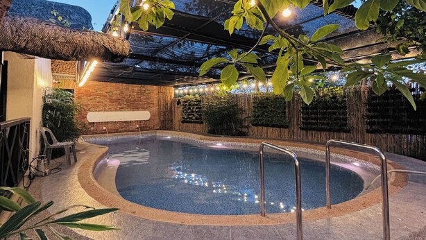 A swimming pool with a stone edge and metal railings, surrounded by greenery and a bamboo fence. - Balai Balatong (Laoag)
