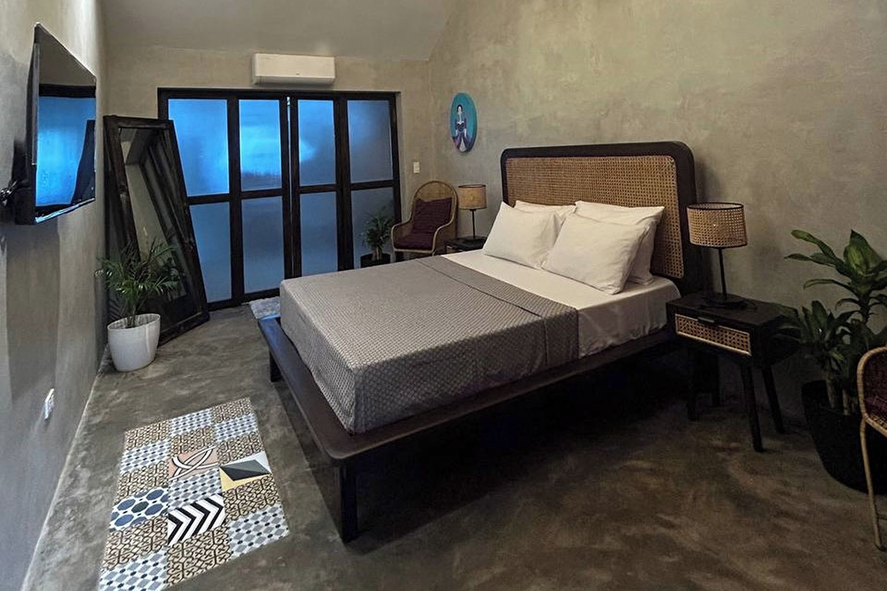 A bedroom with a bed, a TV, a chair, a lamp, and a potted plant.