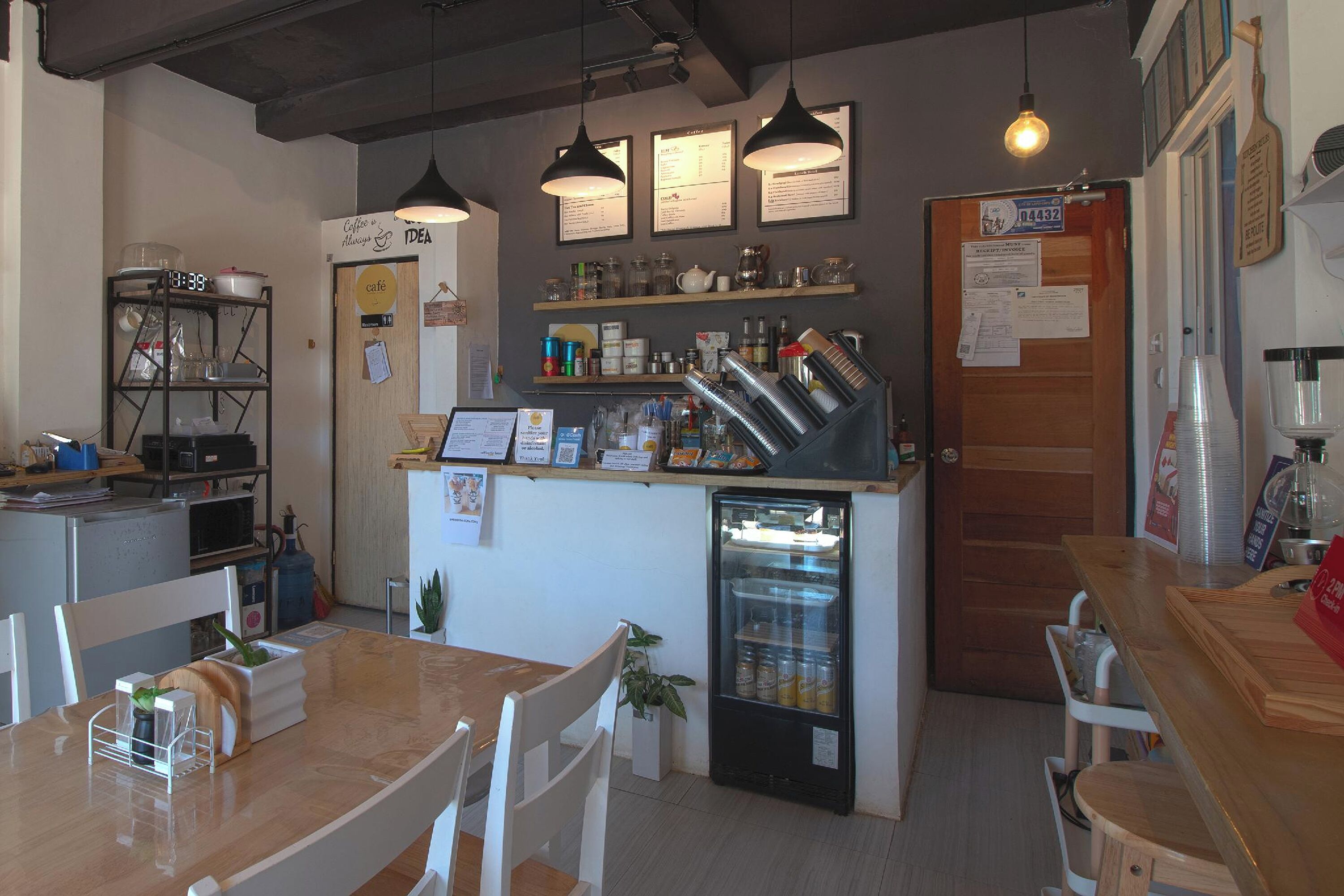 A café with a wooden counter, shelves with various items, a refrigerator, and hanging lights.