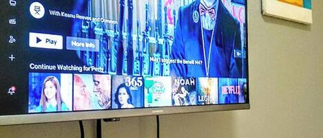 Un televisor de pantalla plana montado en la pared que muestra una interfaz de servicio de streaming con diversas opciones de contenido.