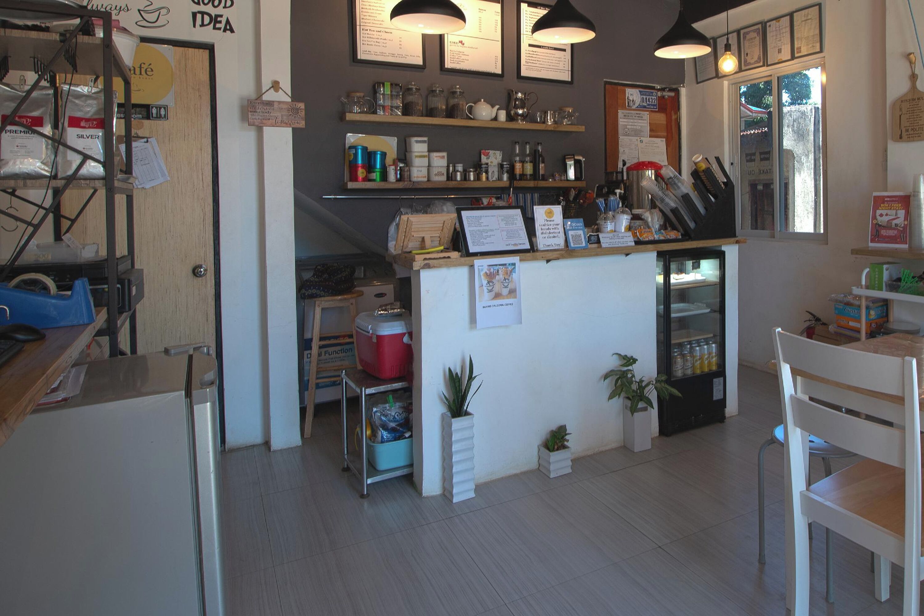Ett café med en bardisk, hyllor med olika varor, ett kylskåp och ett fönster.