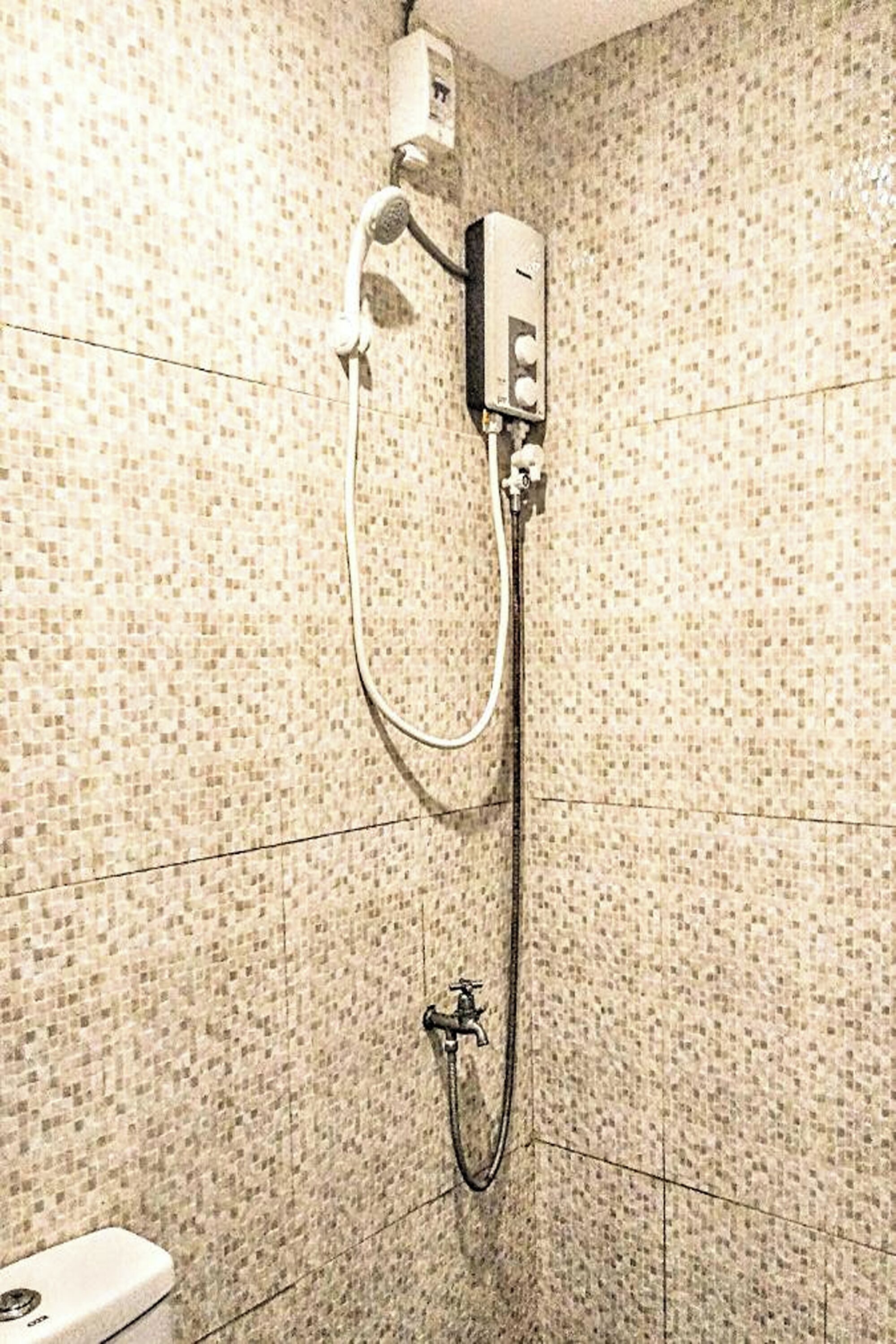 A bathroom with mosaic tile walls, a shower with a handheld showerhead, and a toilet.