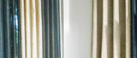Una habitación pequeña con una mesa y dos taburetes, una ventana con cortinas y un equipo de aire acondicionado en la pared.