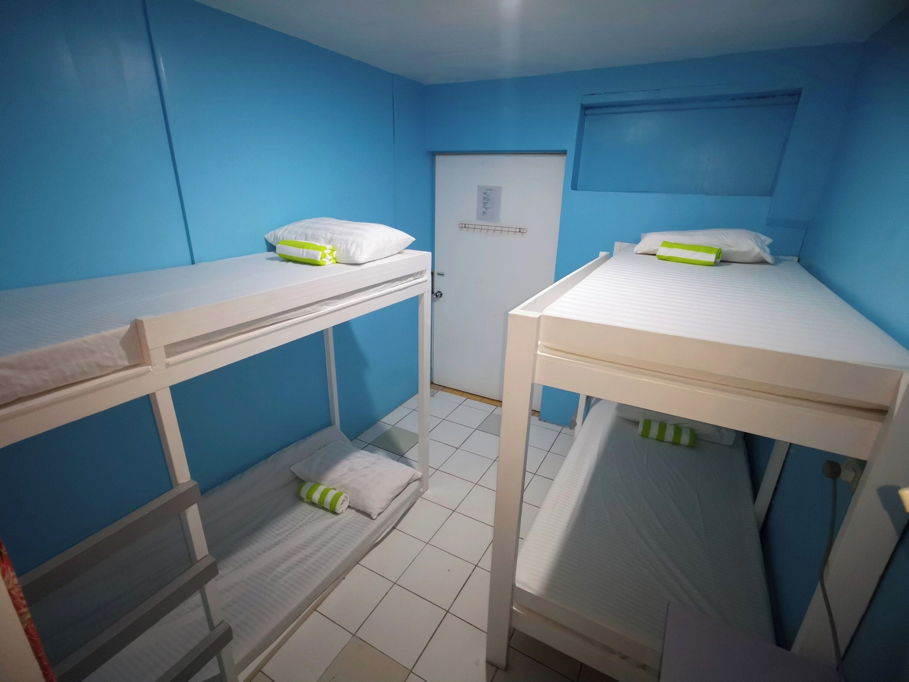 A dormitory room with bunk beds, a white door, and a small window.