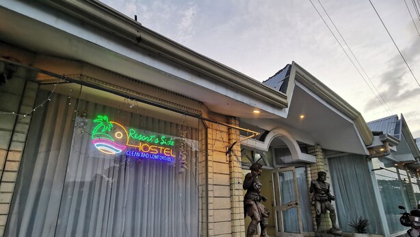 A hostel with a neon sign advertising 'Resort's Side HOSTEL CLEAN AND COMFORTABLE'.