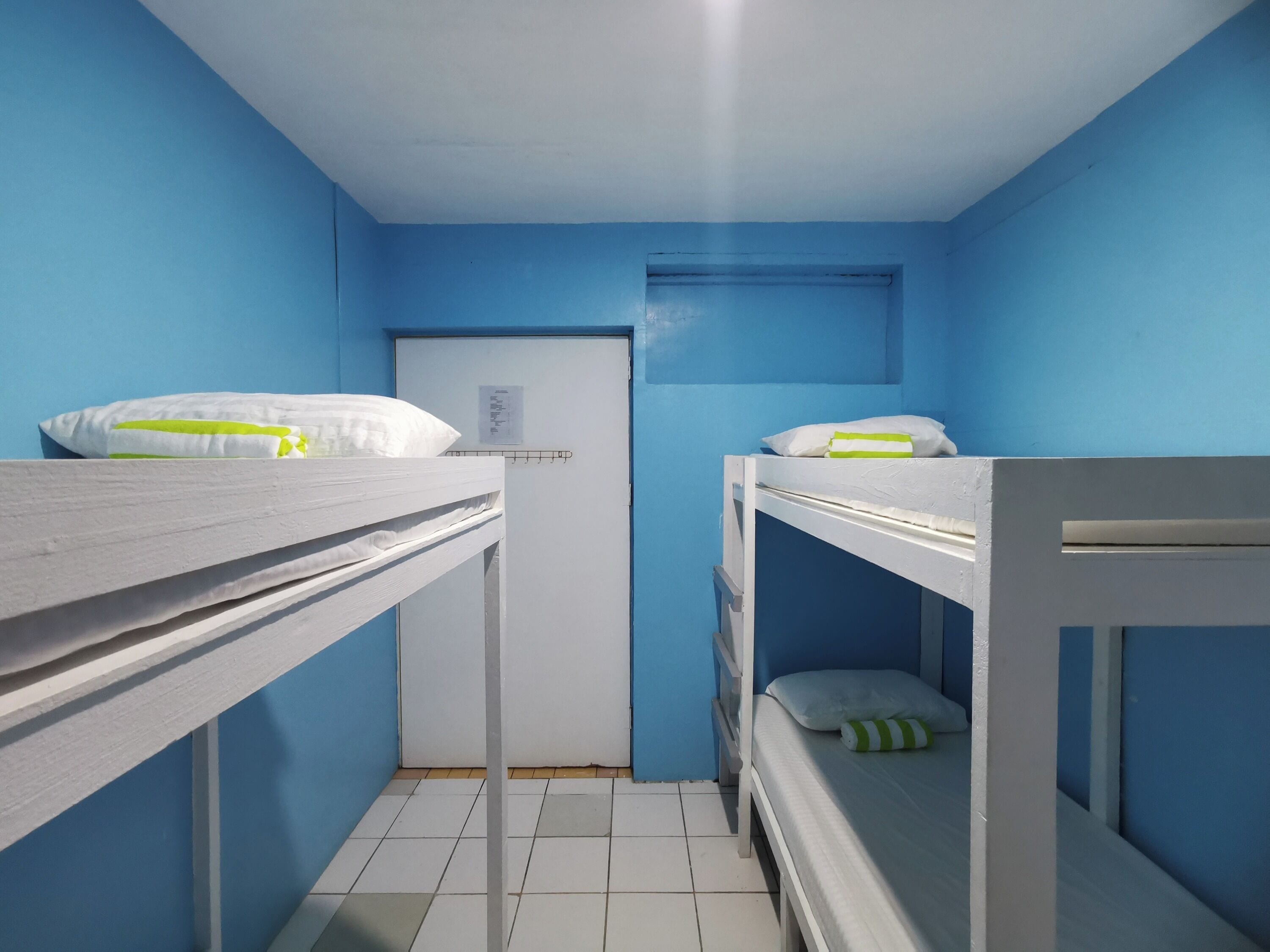 A dormitory room with bunk beds, a door, and a small window.