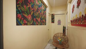 A hallway with a colorful floral mural, a door with a 'Bathroom Rules' sign, and a wicker chair with a vase of flowers.