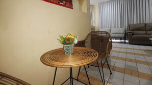 A living room with a round table, two wicker chairs, a sofa, and a decorative wall hanging.