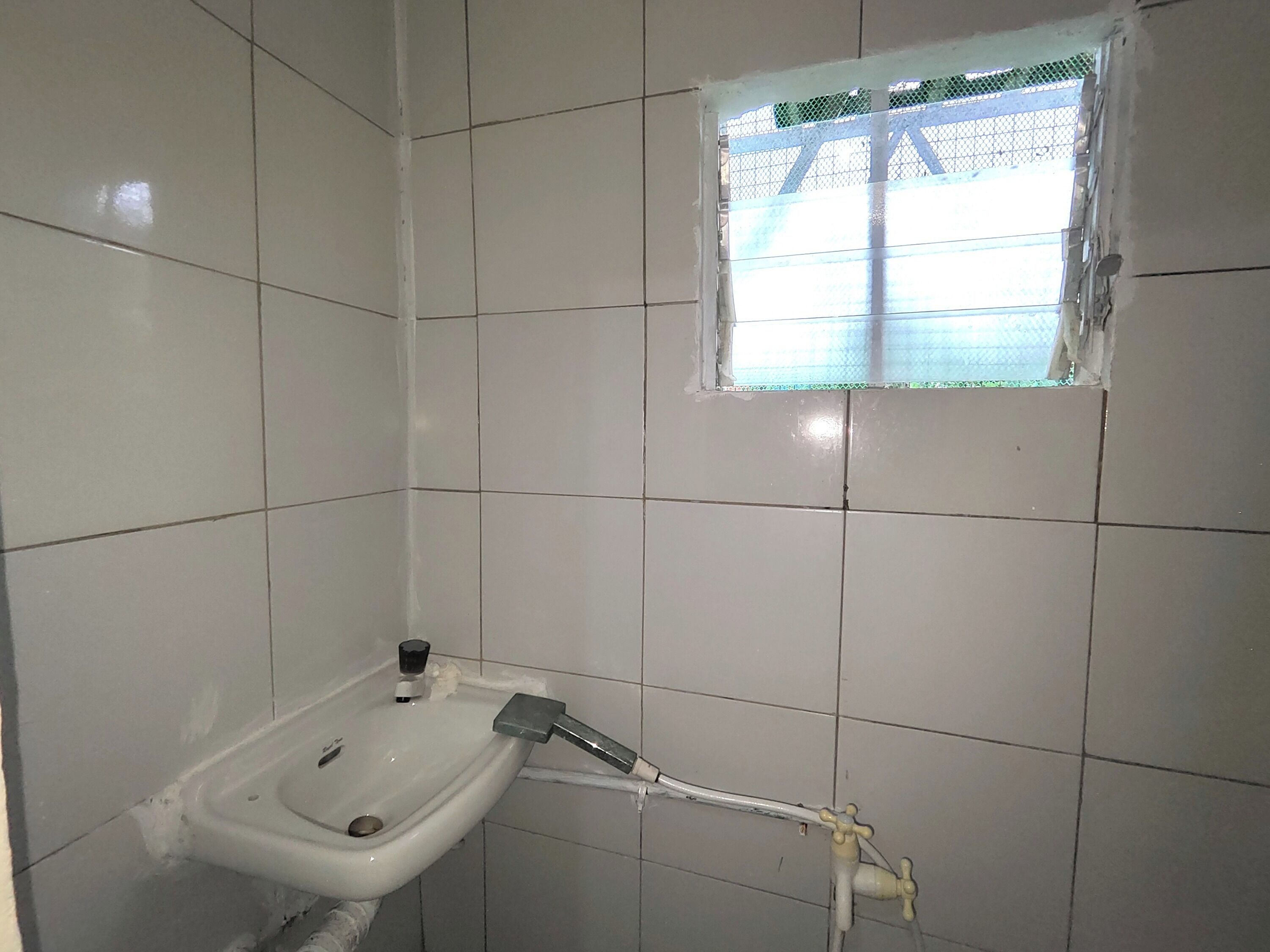 Une salle de bain avec des carreaux blancs, un lavabo et une fenêtre avec une grille en métal.