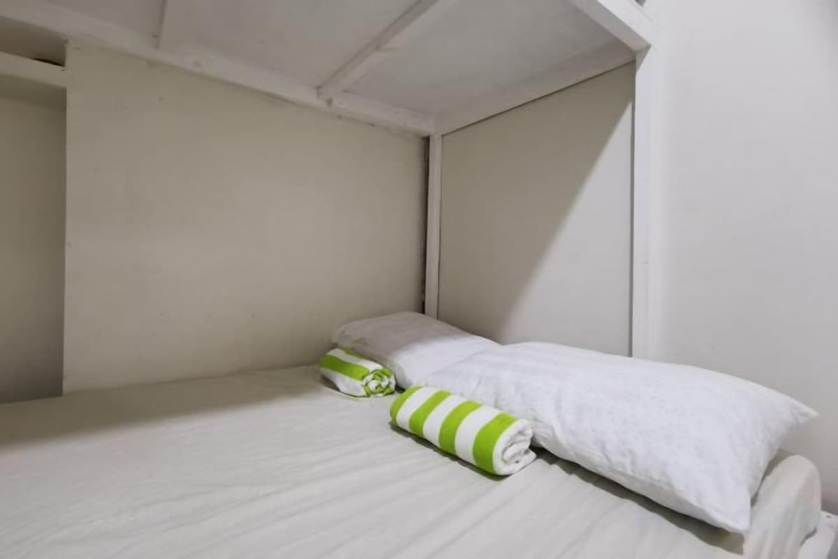 Un lit simple avec une literie blanche et un oreiller à rayures vertes.