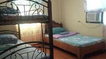 Una habitación con una cama litera y una cama individual. Hay una ventana con cortina y un equipo de aire acondicionado montado en la pared.