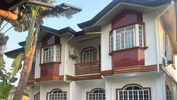 Stylish two-story building with a red accent facade, featuring a balcony and a garden.