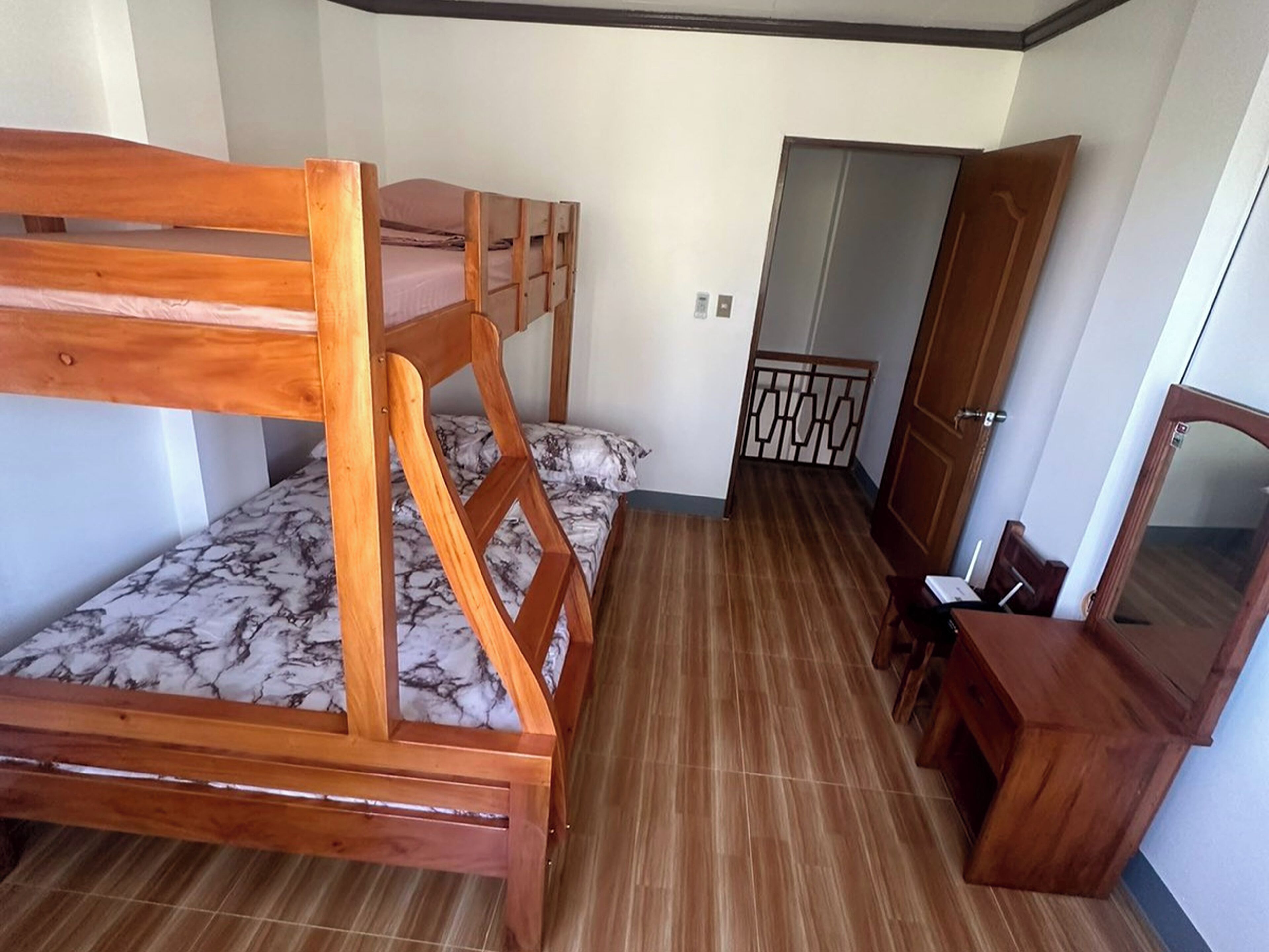 A room with a wooden bunk bed, a small desk with a chair, and a wardrobe.