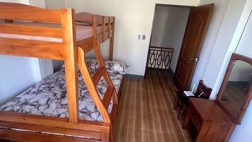 A room with a wooden bunk bed, a small desk with a chair, and a wardrobe.