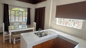 A kitchen with a central island, a built-in sink, and a window with curtains. - Keps Boarding House (San Fernando)