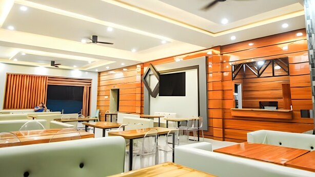 Interior moderno de restaurante com painéis de madeira, mesas brancas e de madeira, e ventiladores de teto.