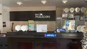 Uma receção de hotel com uma placa que diz "HOTEL PARAGON". Há várias placas informativas e uma pequena vitrine com objetos.