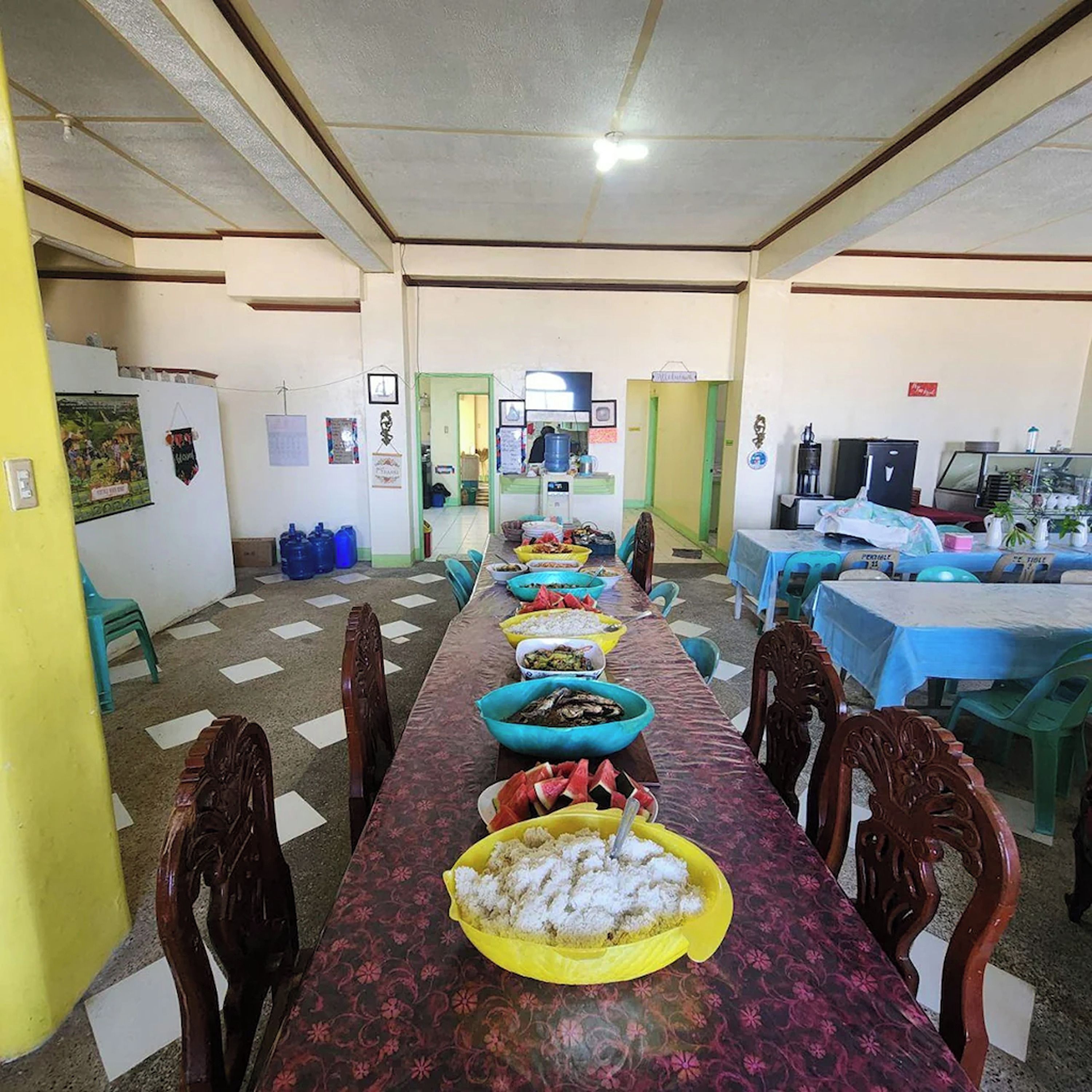 A long dining table with various dishes, chairs, and a kitchen area in the background.