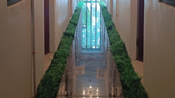A hallway with a shiny, reflective floor, air conditioning units on the walls, and a green plant border. - Hotel Villarte Fort Pampanga (San Fernando)