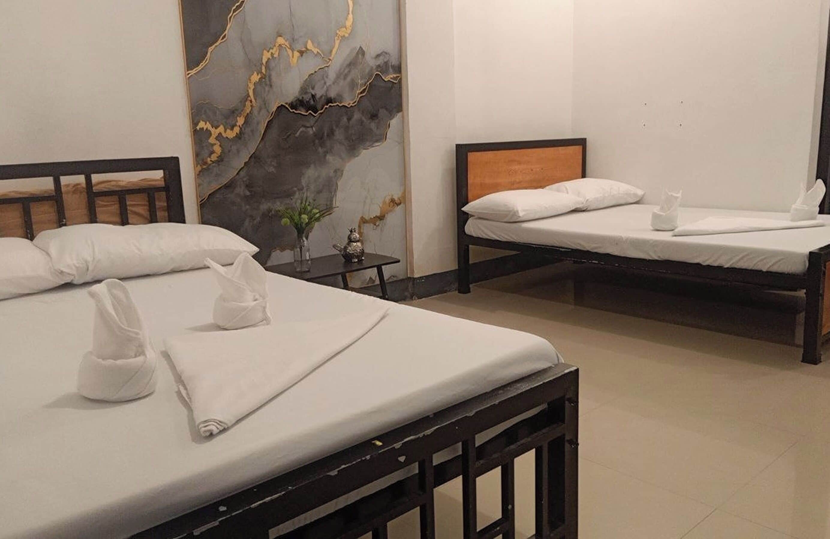 A hotel room with two beds, a marble wall, and a small table with a vase.