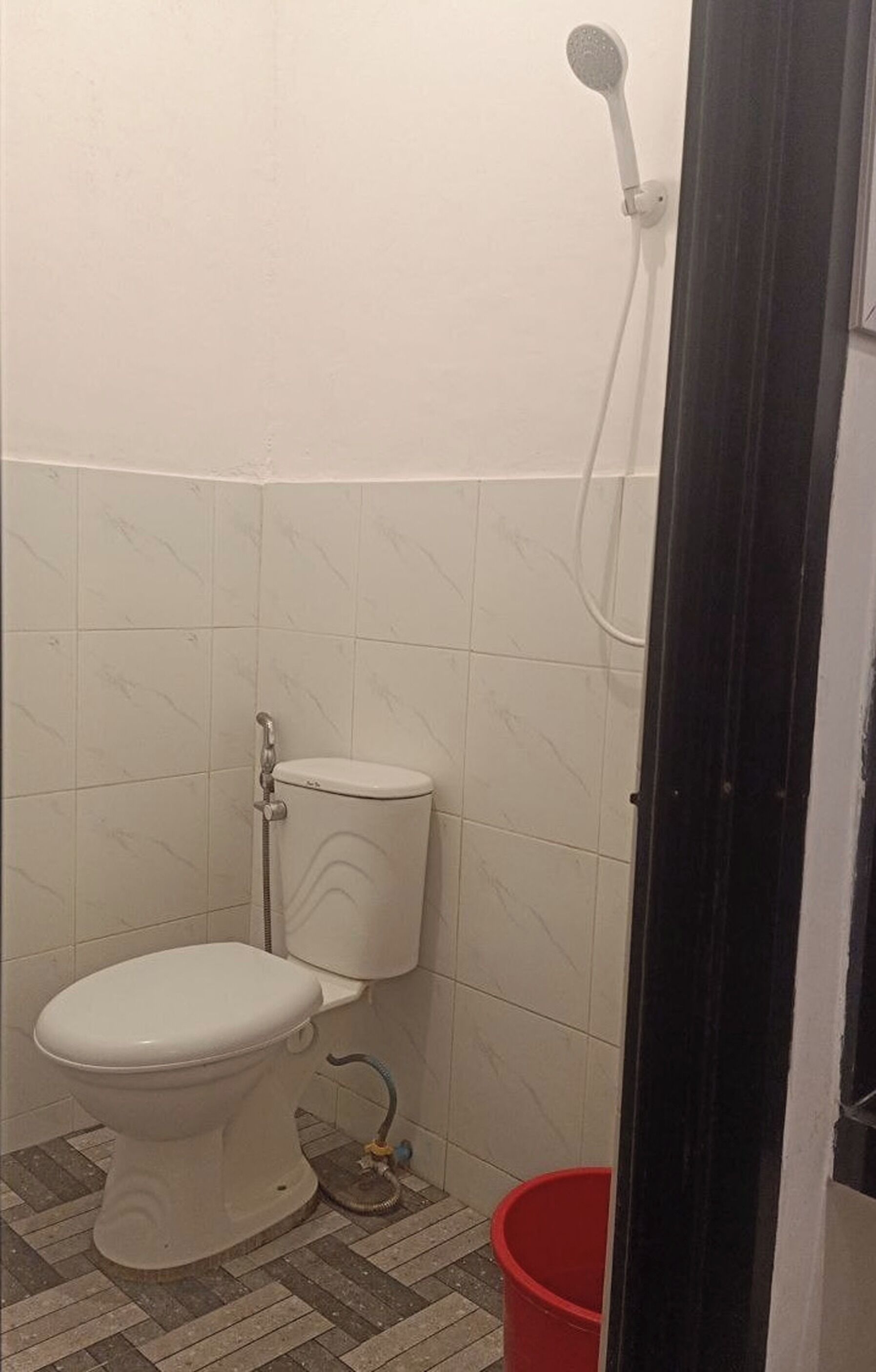 A small bathroom with a toilet, a shower, and a red bucket.