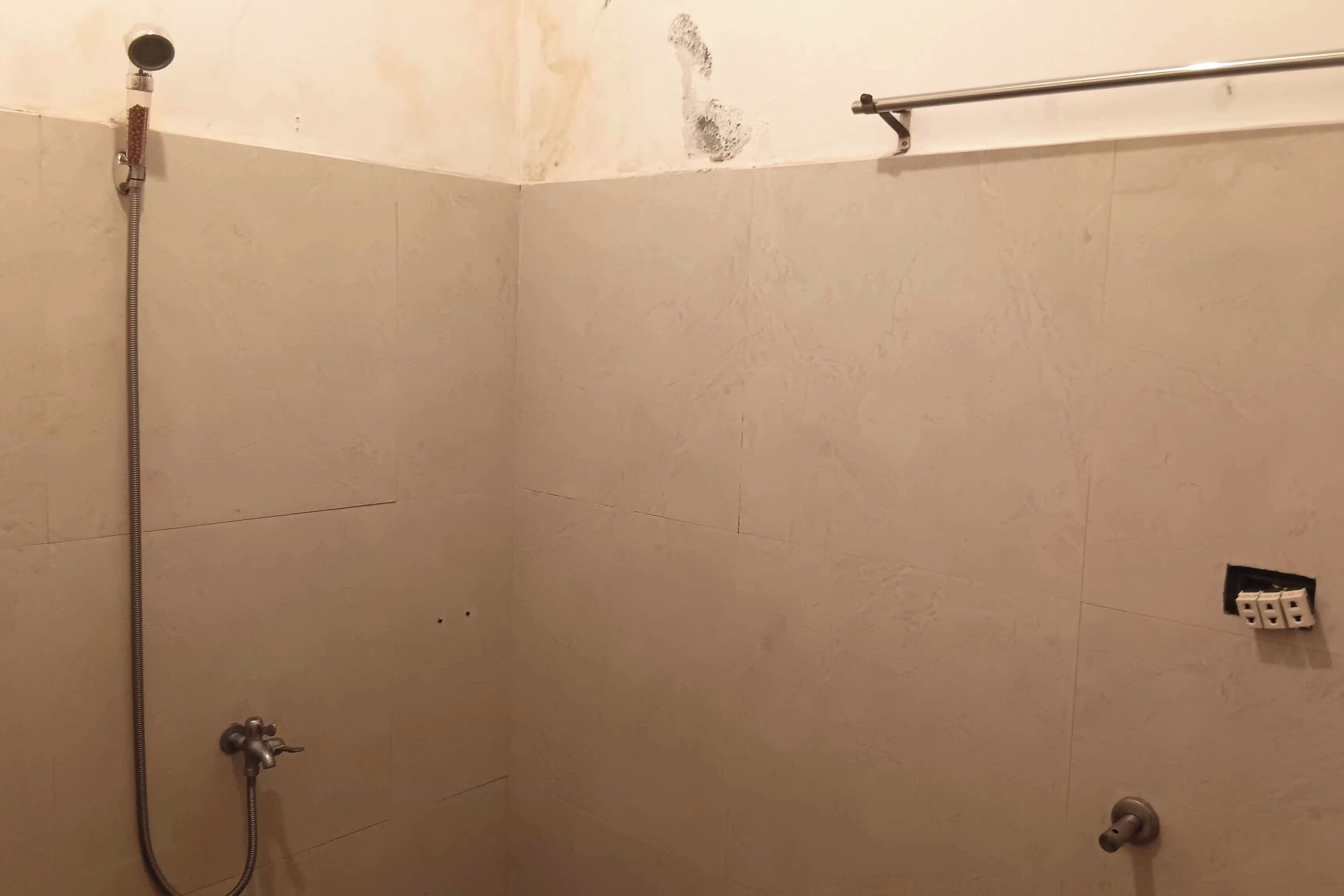 A shower area with a handheld showerhead, a wall-mounted control, and a visible electrical outlet.