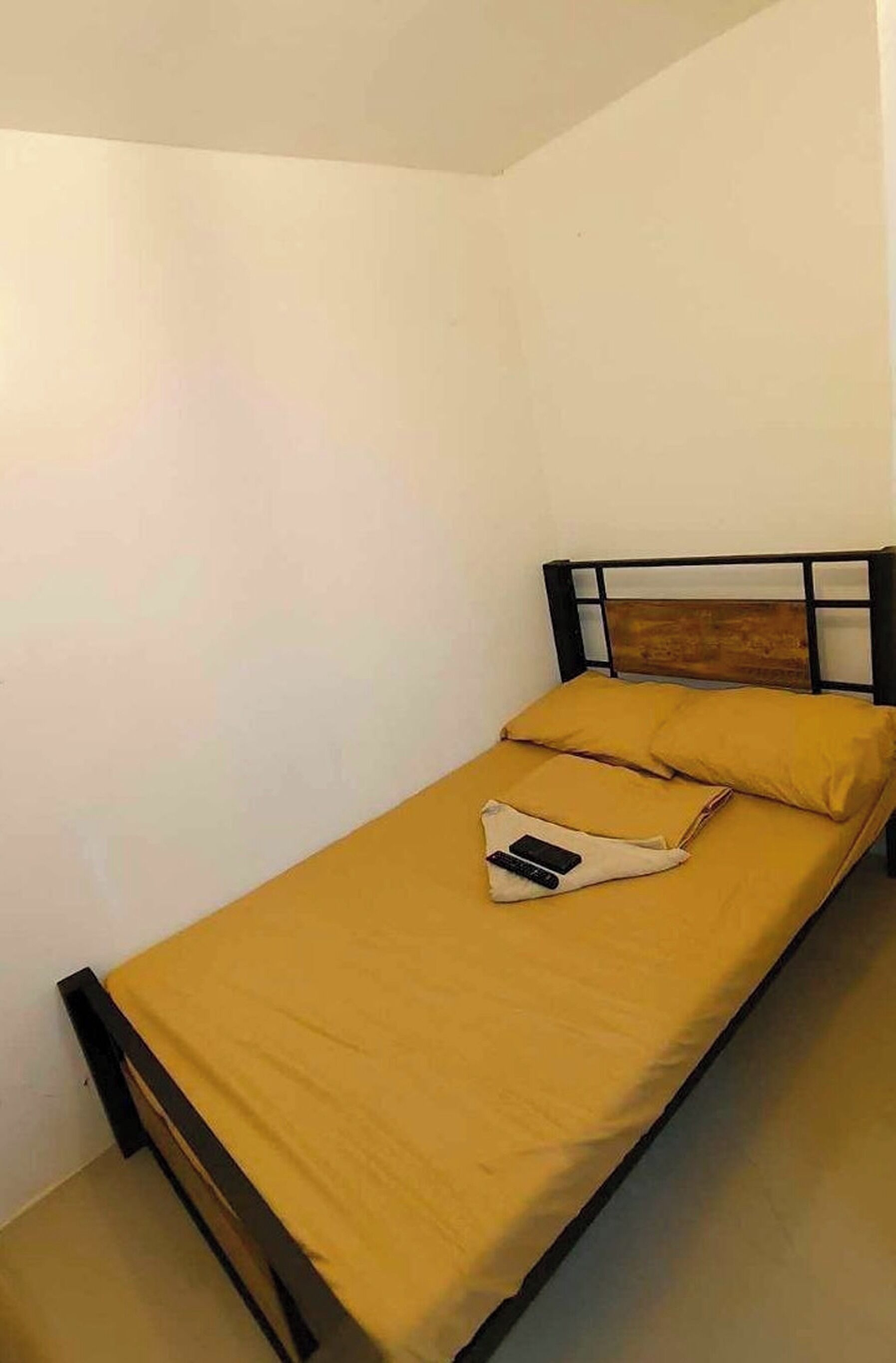 Una cama individual con cabecera de madera, una colcha amarilla y una almohada.
