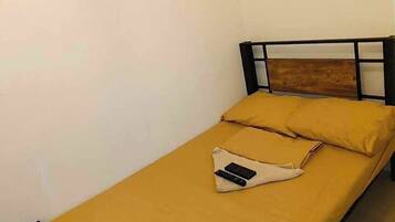 Una cama individual con cabecera de madera, una colcha amarilla y una almohada.