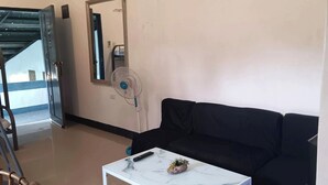 A room with a black sofa, a white marble coffee table, a remote control, a small plant, and a wall-mounted fan. - Hotel Villarte Fort Pampanga (San Fernando)