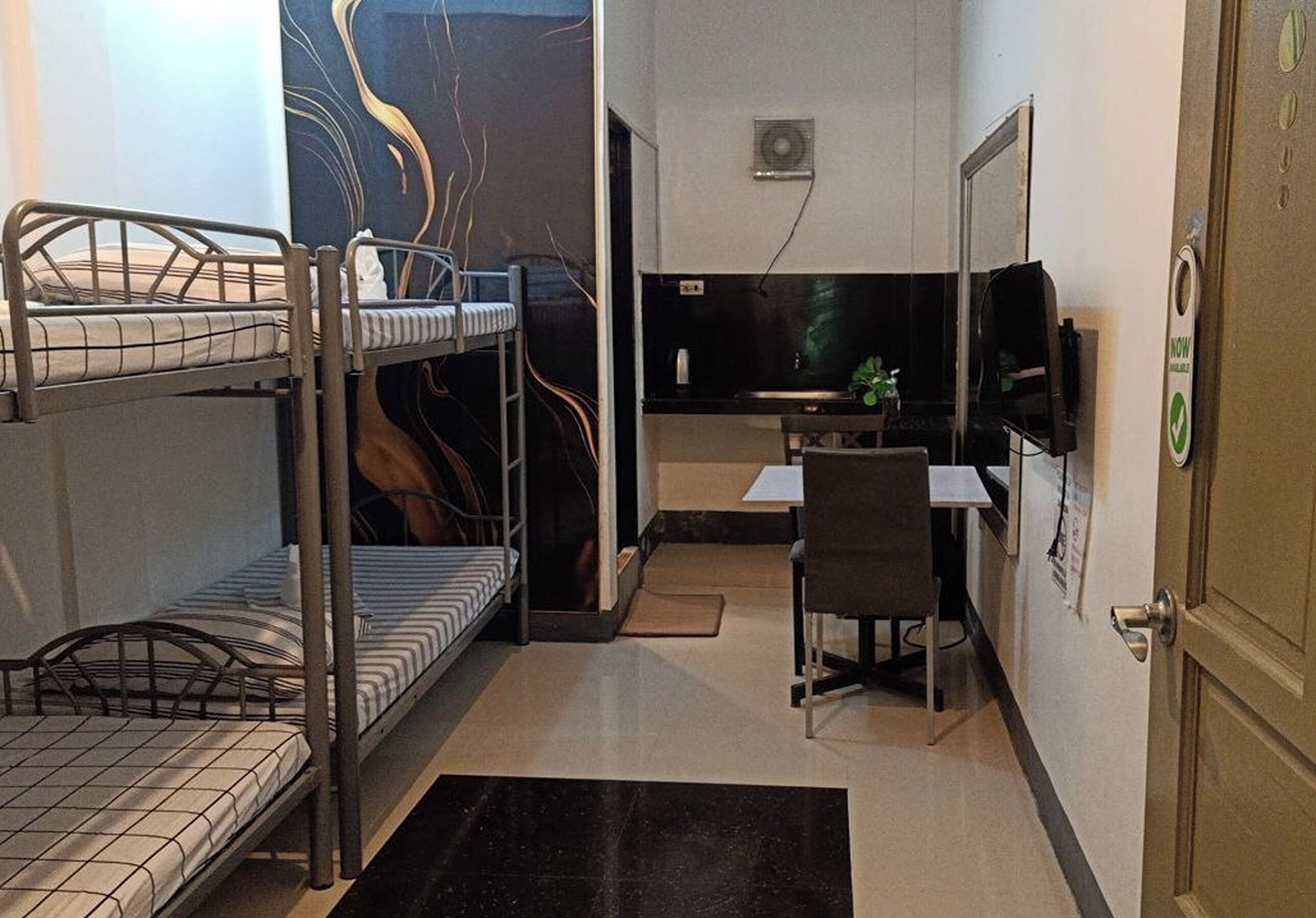 A dormitory room with bunk beds, a desk, a chair, and a television.