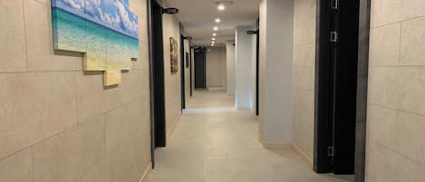 A hotel hallway with numbered doors, a tiled floor, and a painting of a beach scene on the wall.