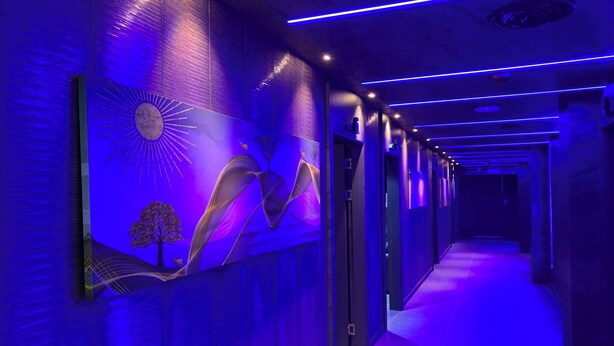 A hallway with a modern design, featuring a sun and tree mural on the wall, and a blue-lit ceiling. - Hotel Kaya Puerto Galera (Puerto Galera)