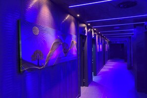 Un couloir au design moderne, orné d’une fresque murale représentant un soleil et un arbre, et doté d’un plafond éclairé d’une lumière bleue.