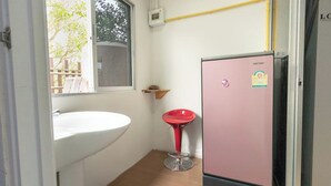 A compact bathroom with a white sink, a pink refrigerator, and a red stool.